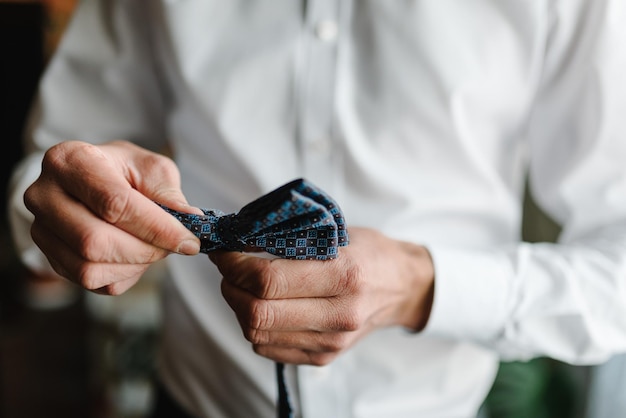 Man dressing bow tie on a shirt in the room clothing concept The groom on the wedding morning Close up