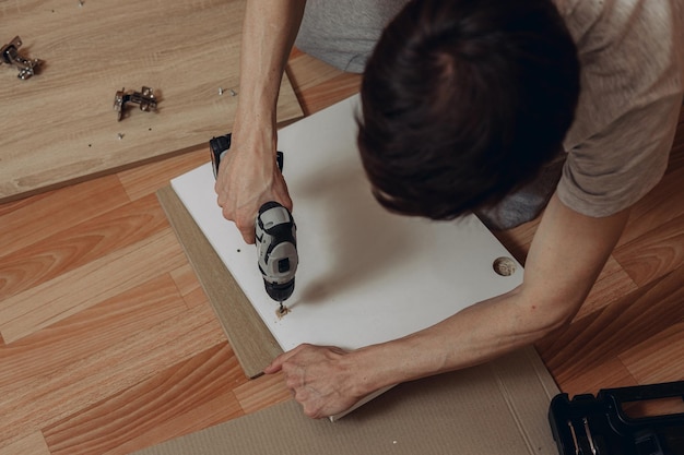 現代の電動ドライバーを使用しながら木の板に穴を開ける男