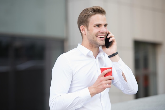 Man drink coffee speak phone urban background. Drink coffee. Each sip is moment of self care. Reasons entrepreneurs drink coffee. Coffee break concept. Relax and pleasure. Call friend share news.