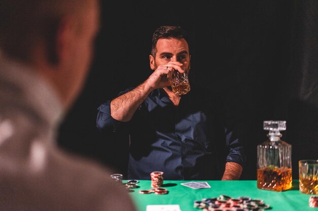 Foto uomo che beve alcol mentre gioca a poker