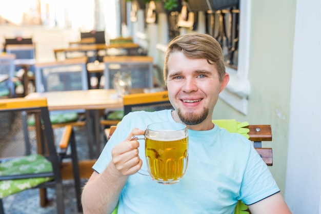 맥주를 마시는 남자. 야외 바에 앉아 맥주를 마시는 잘생긴 젊은 힙스터 남자