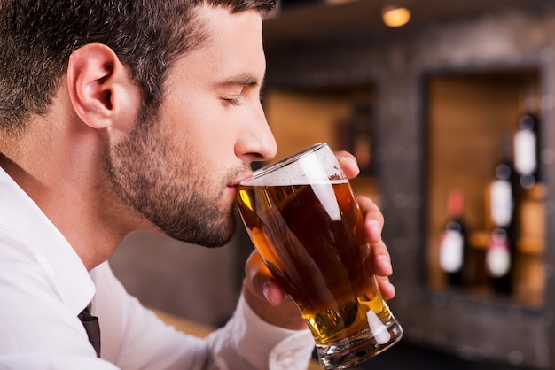 Uomo che beve birra. vista laterale di un bel giovane che beve birra mentre è seduto al bancone del bar