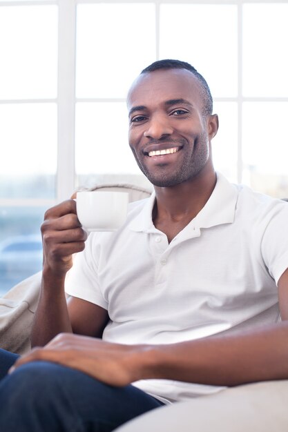 Мужчина пьет кофе. Веселый африканский мужчина пьет кофе и улыбается