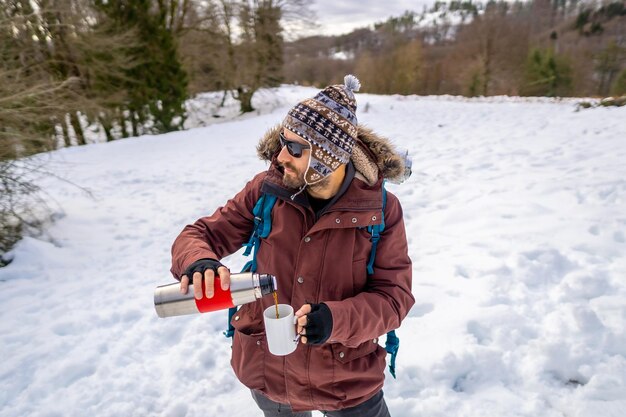 トレッキングを始める前に、雪の中で冬に熱い魔法瓶からコーヒーを飲む男性