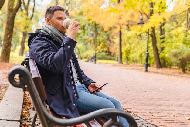 Мужчина пьет кофе на открытом воздухе осенний сезон, разговаривает по телефону