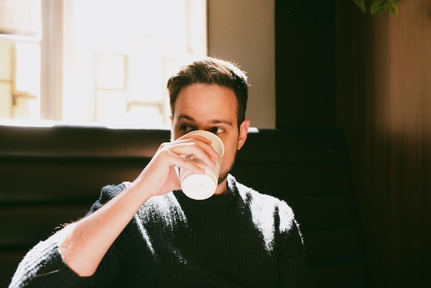 Man drinking coffee in a paper cup inside a coffee shop