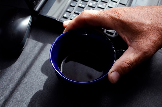 ラップトップで仕事中にコーヒーを飲む男