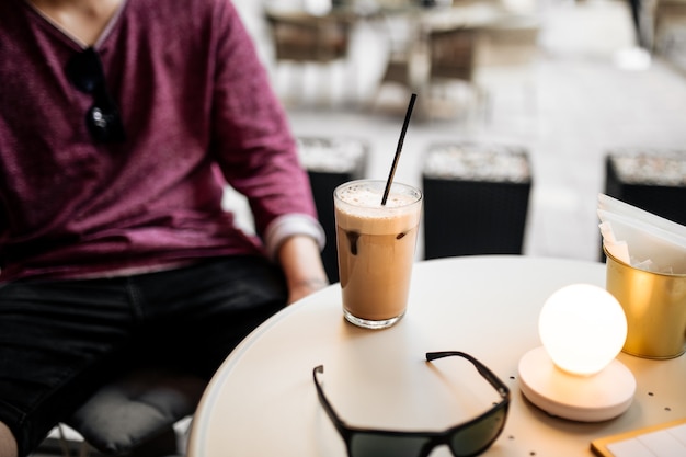 カフェの夏のテラスに座ってラテコーヒーを飲む男