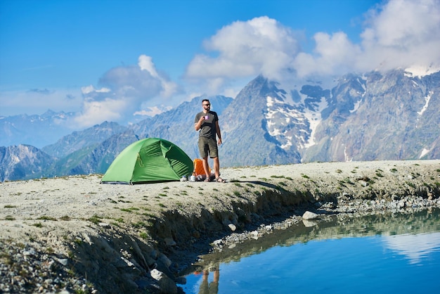 Uomo che beve tè vicino alla tenda in montagna