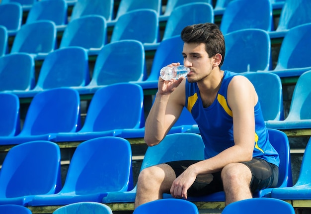 Uomo di acqua potabile da una bottiglia su una tribuna sportiva