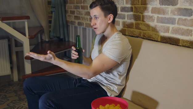 L'uomo beve birra e patatine guardando il calcio.