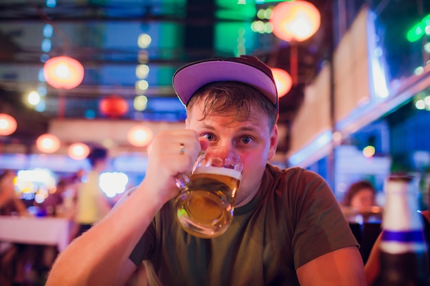 男はビールを飲みます。バーのカウンターに座ってラガーパイントを飲んでハンサムな若い男の側面図