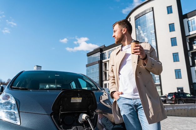 L'uomo beve il caffè mentre carica la sua auto elettrica