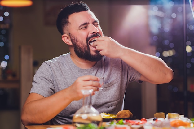 Man drinks vodka at a large table with food and snacks fat.