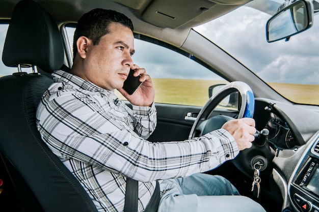 차 안에서 전화를 거는 남자 운전사 운전 중 전화를 거는 남자의 개념 휴대 전화를 사용하여 차 안에 앉아 있는 젊은 남자의 측면 보기