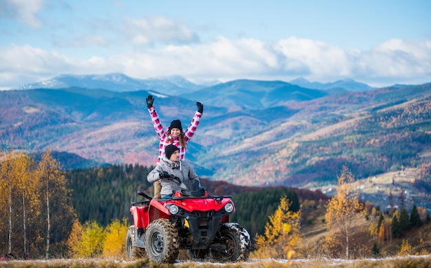 Man driving atv quad bike, woman sitting behind him and raised her hands up on a mountain road