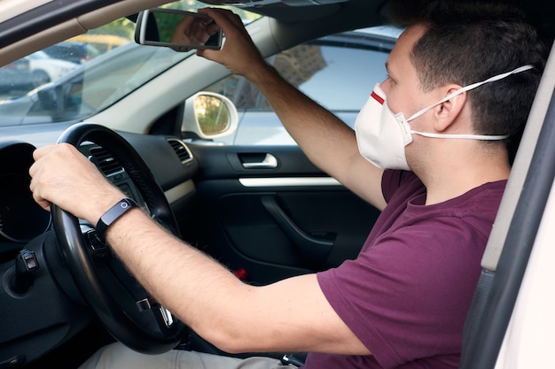 Un uomo alla guida di un'auto con una maschera medica durante un'epidemia