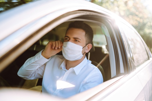 L'uomo alla guida di un'auto indossa una mascherina medica durante un'epidemia nella città di quarantena.