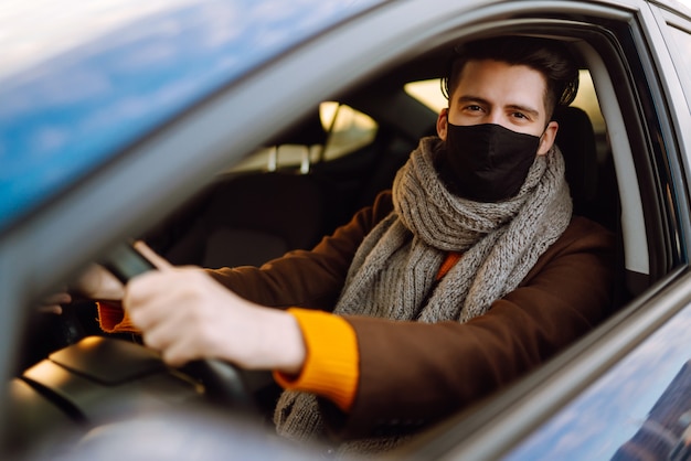 流行中に医療用マスクを着用して車を運転している男性。トランスポートの分離。 Covid-2019。