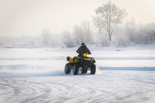 冬の野原でクワッドバイクを運転する男 雪の中で冬に ATV のギアを入れた極端なモトライダー 雪の吹きだまり ATV が曲がり角で横滑りした