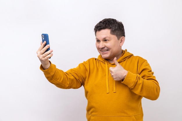 Man duimen opdagen als gebaar en kijken naar telefooncamera selfie maken of video opnemen