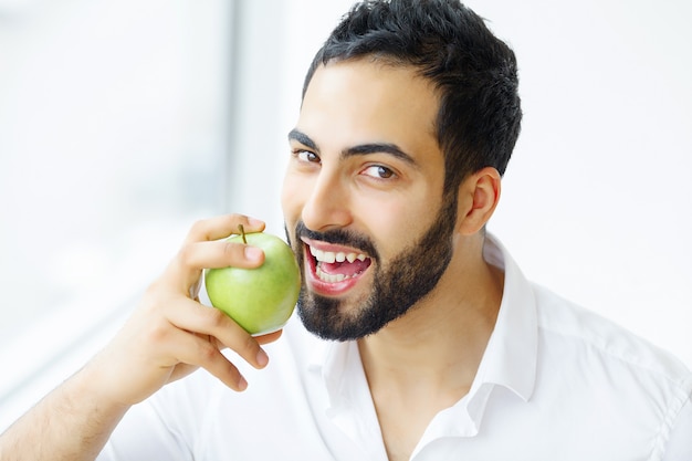 Человек ест яблоко. Красивая девушка с белыми зубами кусая яблоко. Изображение высокого разрешения