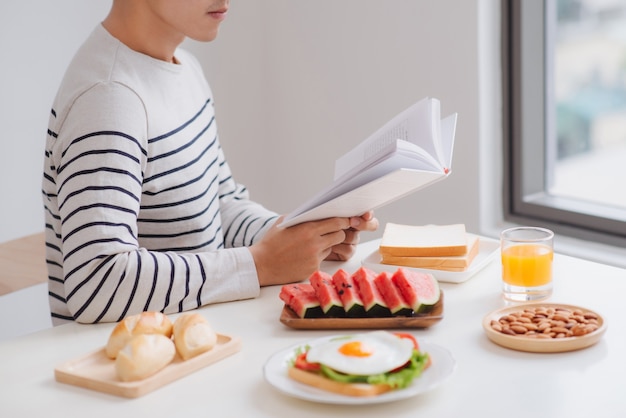 朝、家で朝食を食べて本を読んでいる男性。