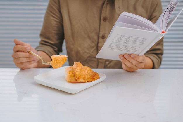 Uomo che fa colazione e legge un libro mentre è seduto a un tavolo bianco