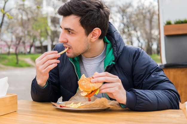 Man eating fried potatoes with a burger in street food cafe