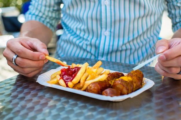 man eating German Currywurst at stand