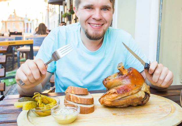 豚肉のナックルを食べてビールを飲む男