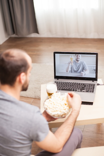 自己隔離中に友人とのビデオ通話中にポップコーンを食べる男。