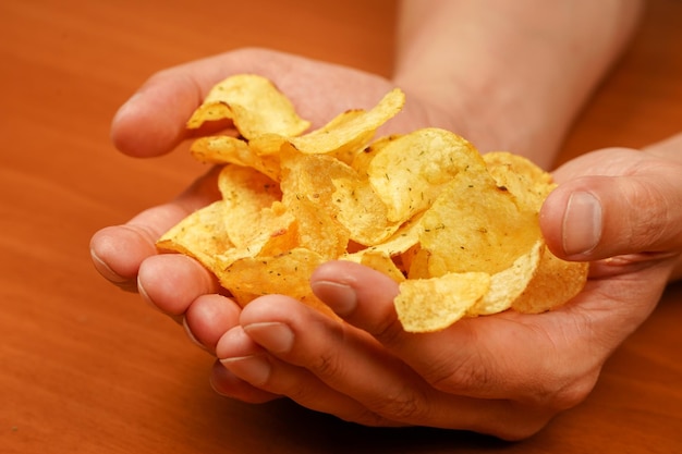 ポテトチップスを食べている男 手にポテトチッピスを握っている手の見た目 ひっくり返したポテトシップスの山を握っている手 ファストフード ジャンクフード 不健康なライフスタイル カロリー 肥満 アメリカの食事