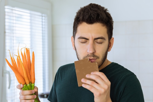 Man eats chocolate with great pleasure. He does not want to eat vegetables.