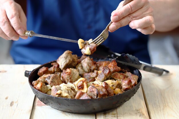 A man eats pieces of meat from a frying pan