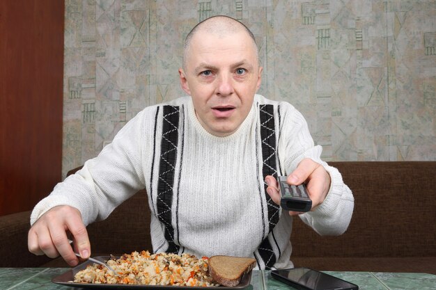 The man eats rice pilaf and stares of TV program