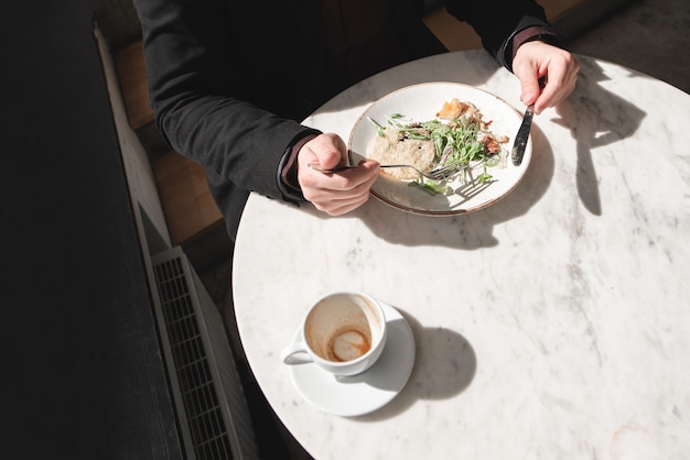 Man eats a salad with a fork and a knife in his hands.