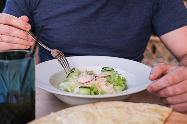 Un uomo mangia un'insalata con cetrioli calamari e verdure con salsa di ostriche in un caffè