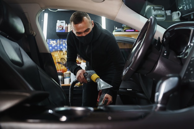 Man een auto stofzuigen. Werknemer desinfecteert auto. Werk van detaillering in quarantaine