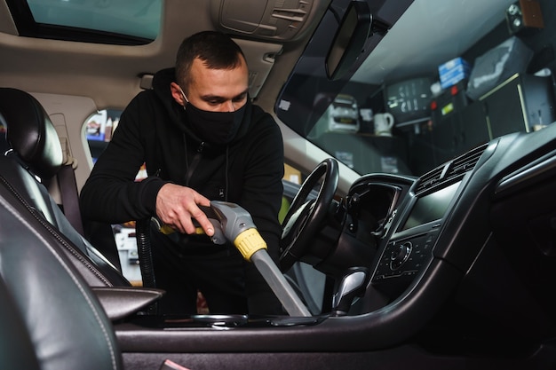 Man een auto stofzuigen. Werknemer desinfecteert auto. Werk van detaillering in quarantaine