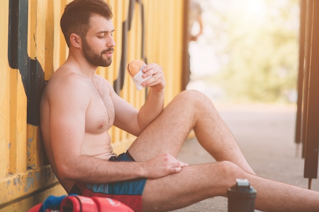 Man eet een hamburger na een training. Zeer hongerig, vet en ongezond voedsel.