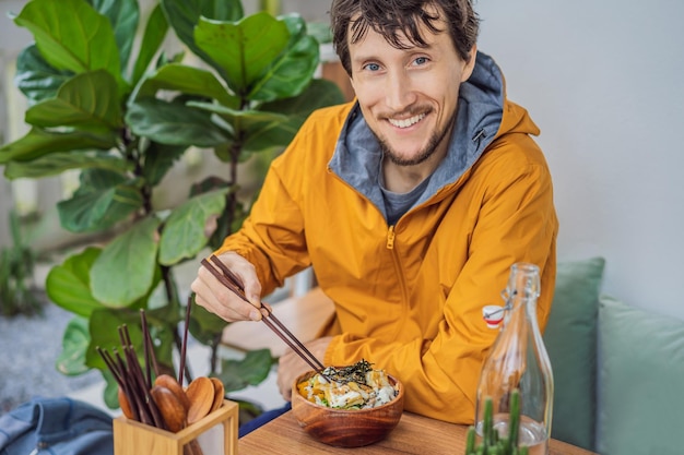 Man eet rauwe biologische poke bowl met rijst en groenten close-up op het tafelblad van bovenaf bekijken