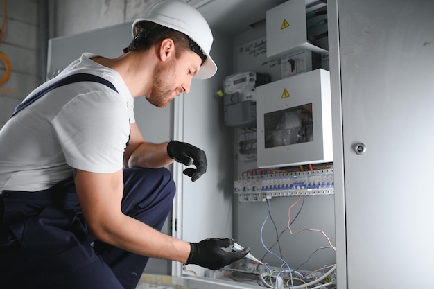 Man an electrical technician working in a switchboard with fuses Installation and connection of electrical equipment Professional with tools in hand concept of complex work space for text