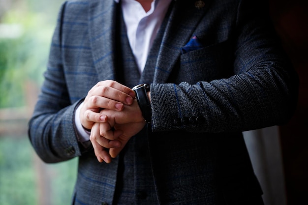 男性のエレガントなビジネスマンは彼の手に時計をボタンで留めます彼は白いドレスシャツを着ています