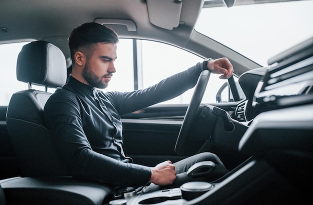 Man in elegant clothes sitting in brand new expencive automobile.