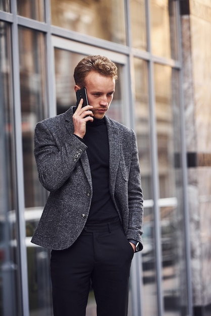 電話で話しているモダンな建物に対して外でエレガントなフォーマルな服装の男。