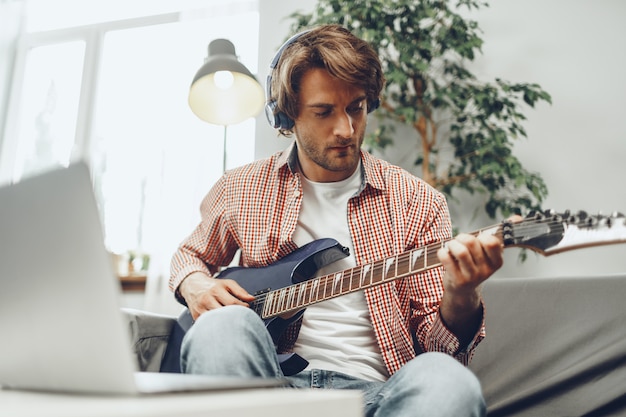 Man elektrische gitaar spelen en muziek opnemen in laptop