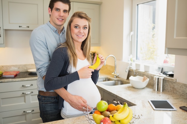 Uomo che abbraccia la moglie incinta che tiene una banana