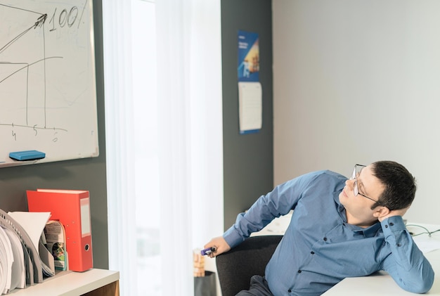 Man employee in blue shirt and glasses sitting at the desk in office watching on the graph on white board Business busy working day concept