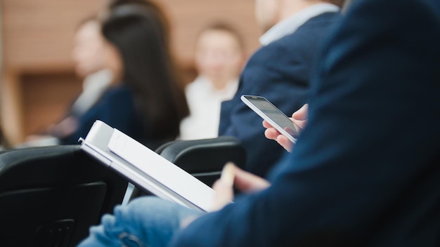 Man employee in suit uses digital device sitting on the forum about industry and economy